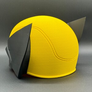 May include: Yellow and black plastic costume helmet with a textured surface. The helmet has a rounded shape with a pointed top and two black ear pieces.
