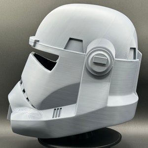 May include: A white plastic helmet with a detailed design, featuring a visor and a side panel with a circular detail. The helmet is a replica of a character from a popular science fiction franchise.