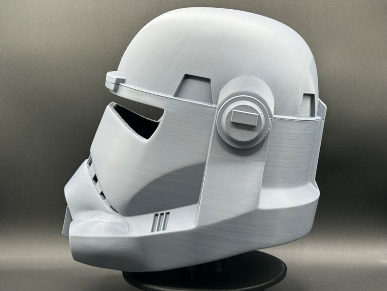 May include: A white plastic helmet with a detailed design, featuring a visor and a side panel with a circular detail. The helmet is a replica of a character from a popular science fiction franchise.