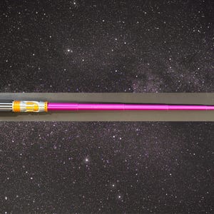 May include: A pink lightsaber with a silver, black, and gold hilt. The lightsaber is displayed horizontally against a starry background. The hilt features intricate details and a metallic finish. The blade is a vibrant pink color.