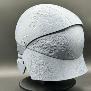 May include: A white, textured helmet with a raised design. The helmet is made of a hard plastic material and has a visor that can be raised or lowered.