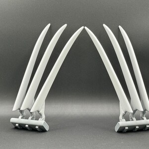 May include: A set of six silver-colored claws, three on each side, with a black base. The claws are curved and pointed, resembling Wolverine's claws.