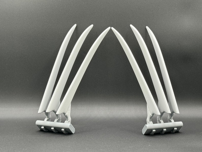May include: A set of six silver-colored claws, three on each side, with a black base. The claws are curved and pointed, resembling Wolverine's claws.