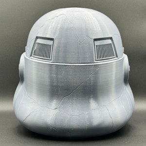 May include: A gray plastic helmet with a textured surface and two rectangular vents on the top. The helmet has a cracked appearance.