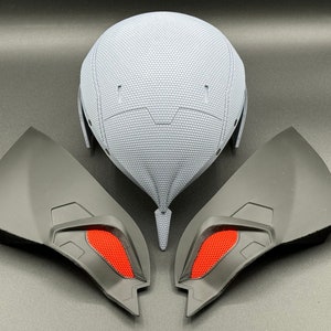 May include: A gray helmet with a textured surface and two black and red wing-shaped pieces.