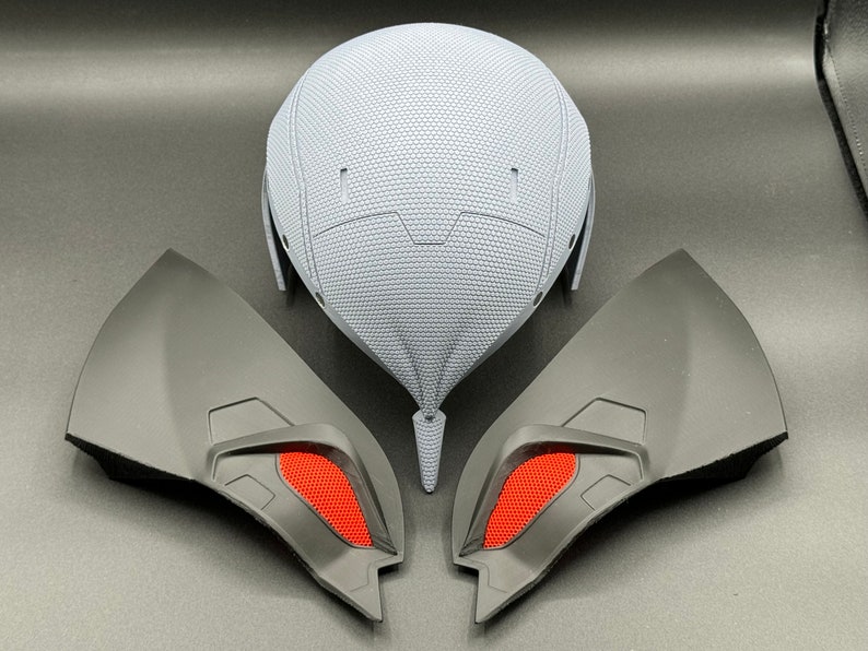 May include: A gray helmet with a textured surface and two black and red wing-shaped pieces.