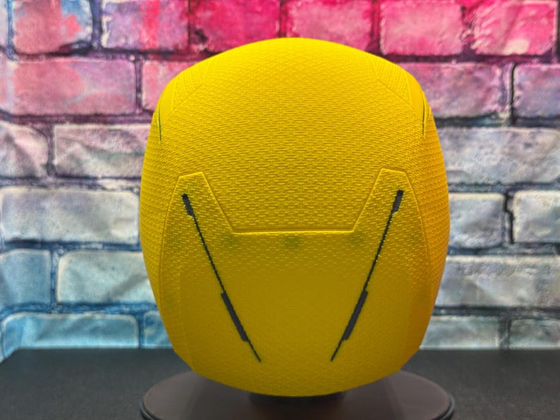 Puede incluir: Casco deportivo amarillo brillante con superficie texturizada y l&iacute;neas negras. El casco se muestra sobre un fondo de pared de ladrillos.