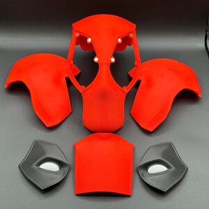 K&ouml;nnte beinhalten: Ein Set aus rot und schwarz 3D-gedruckten Kost&uuml;mteilen f&uuml;r ein Superhelden-Kost&uuml;m. Das Set beinhaltet ein Kopfst&uuml;ck, zwei Schulterst&uuml;cke, ein Brustst&uuml;ck und zwei Augenst&uuml;cke.