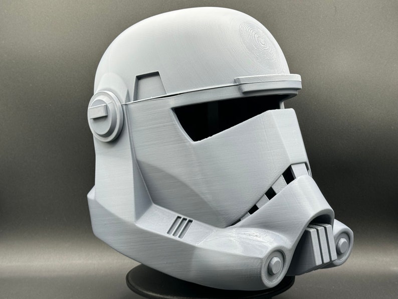 May include: A white plastic 3D printed helmet with a visor and a detailed design. The helmet is a replica of a Star Wars character.