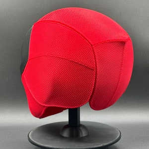 May include: Red and black Deadpool mask with a textured surface. The mask is on a black stand.