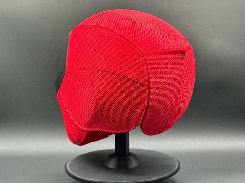 May include: Red and black Deadpool mask with a textured surface. The mask is on a black stand.