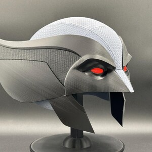 May include: A black and gray helmet with red eyes. The helmet has a textured surface and a sharp, angular design.