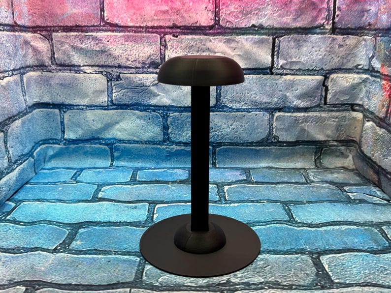 May include: A black hat stand with a round base and a tall, slender pole. The top of the stand has a curved, hat-shaped design. The stand is made of metal and is designed to hold a hat.