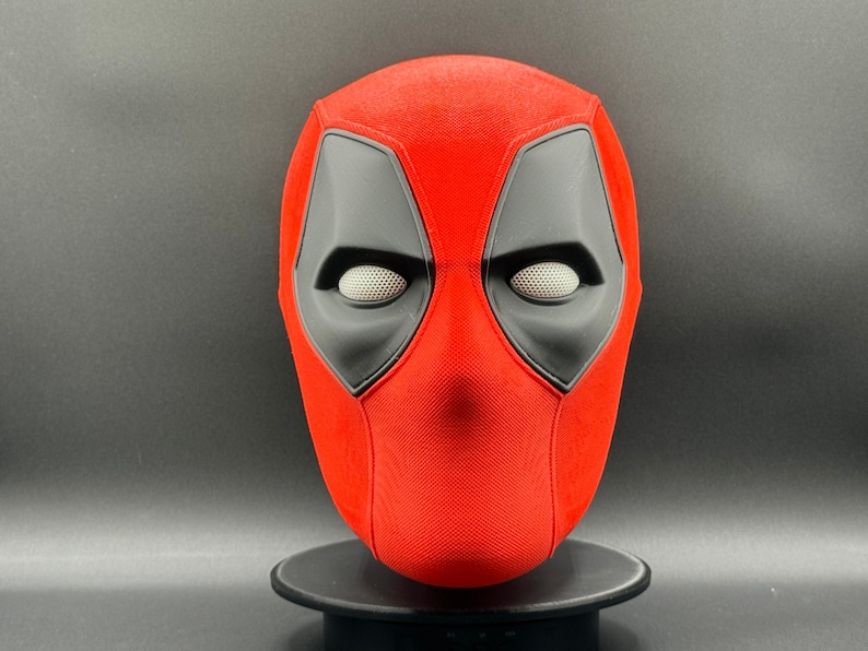K&ouml;nnte beinhalten: Eine rote und schwarze Deadpool-Maske mit strukturierter Oberfl&auml;che. Die Maske hat zwei Augenl&ouml;cher und eine kleine &Ouml;ffnung f&uuml;r den Mund.