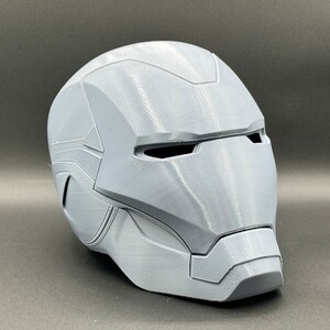 Puede incluir: Un casco gris impreso en 3D con un dise&ntilde;o detallado, que se asemeja al casco de un superh&eacute;roe.