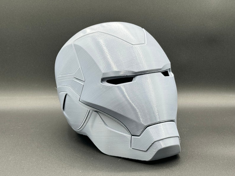 Puede incluir: Un casco gris impreso en 3D con un dise&ntilde;o detallado, que se asemeja al casco de un superh&eacute;roe.