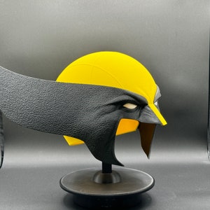 Puede incluir: Una m&aacute;scara de Wolverine de pl&aacute;stico amarillo y negro con una superficie texturizada. La m&aacute;scara est&aacute; en un soporte negro.
