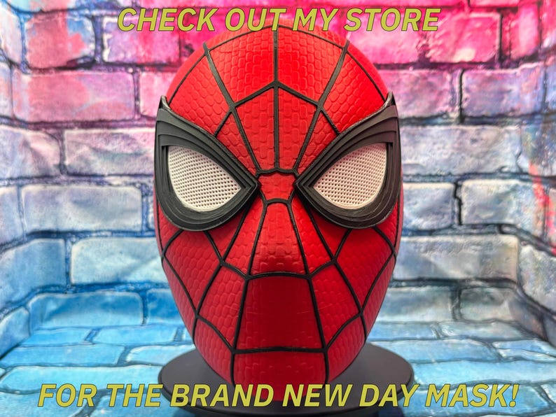 以下が含まれることがあります： 黒いクモの巣と目の詳細が施された赤いスパイダーマンマスク。マスクはテクスチャ加工された表面で、黒いスタンドに展示されています。上部のテキストは「CHECK OUT MY STORE」、下部のテキストは「FOR THE BRAND NEW DAY MASK！」です。
