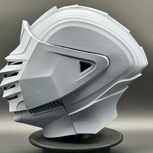Puede incluir: Un casco impreso en 3D con un dise&ntilde;o detallado, que incluye una visera y una superficie texturizada. El casco es gris y parece estar hecho de pl&aacute;stico.