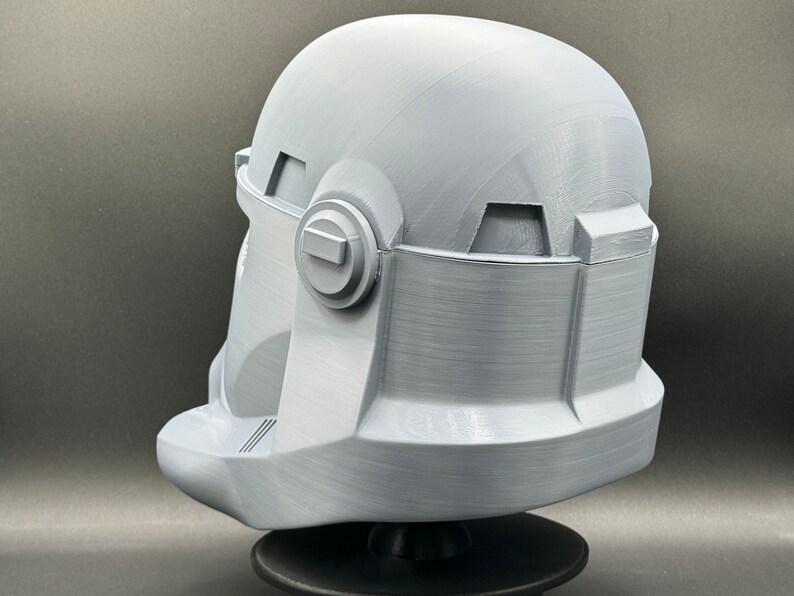 May include: A white plastic 3D printed helmet with a textured surface. The helmet has a visor and a round, raised detail on the side.