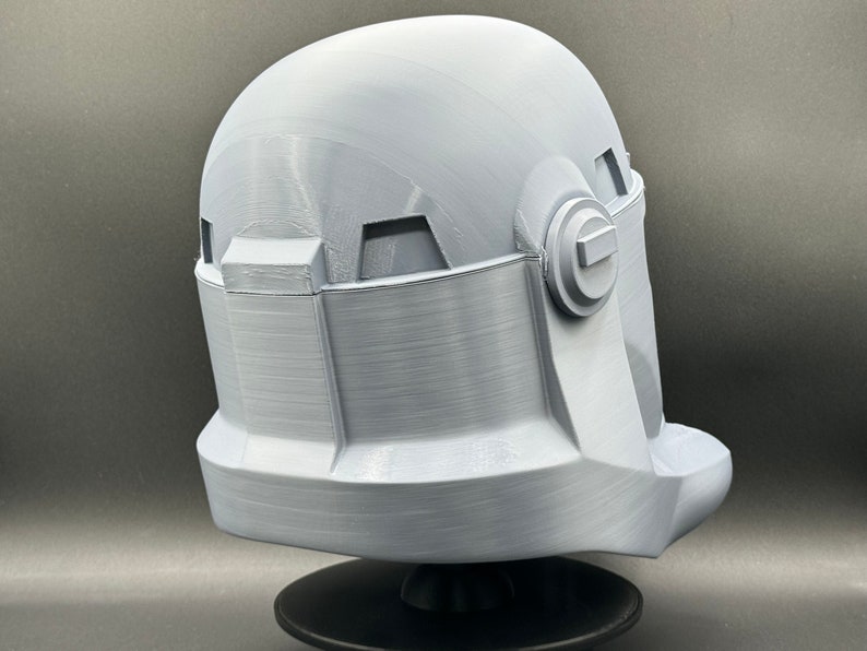 May include: A white plastic helmet with a textured surface and a raised detail on the side. The helmet is on a black stand.