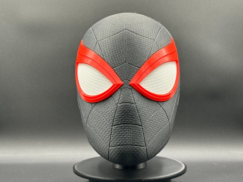 Puede incluir: M&aacute;scara de Spider-Man negra y roja con una superficie texturizada. La m&aacute;scara tiene una malla blanca sobre los ojos.
