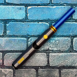 May include: A futuristic-looking, dark gray and blue device with a blue tip, gold accents, and a yellow button. The device has a rectangular section with text and a curved opening. The background is a blue brick wall.