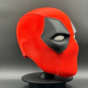 K&ouml;nnte beinhalten: Eine rote und schwarze Deadpool-Maske mit einem detaillierten Augenloch und einer strukturierten Oberfl&auml;che.
