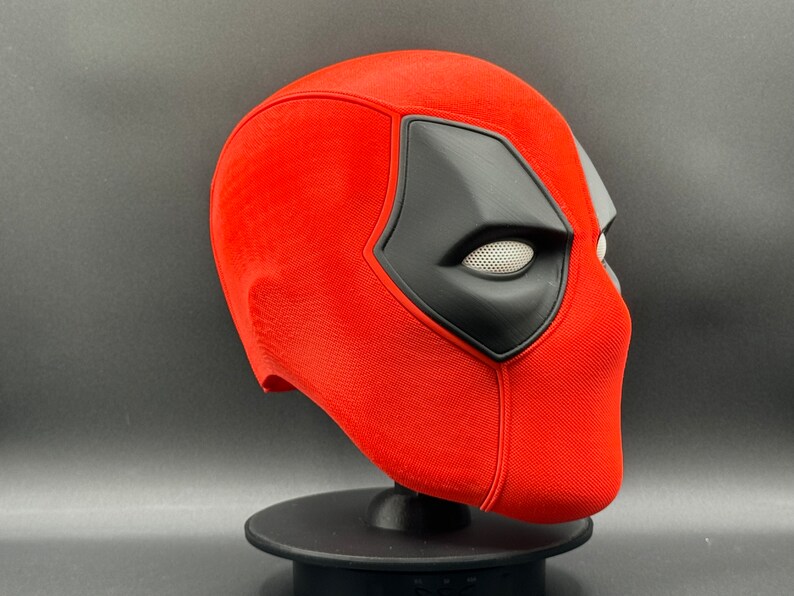 K&ouml;nnte beinhalten: Eine rote und schwarze Deadpool-Maske mit einem detaillierten Augenloch und einer strukturierten Oberfl&auml;che.