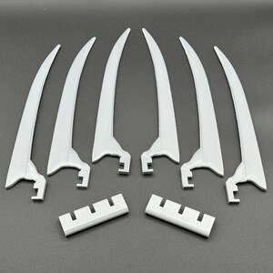 May include: Six white plastic claws with a textured surface and a curved shape. Two white plastic pieces with a textured surface and a rectangular shape.