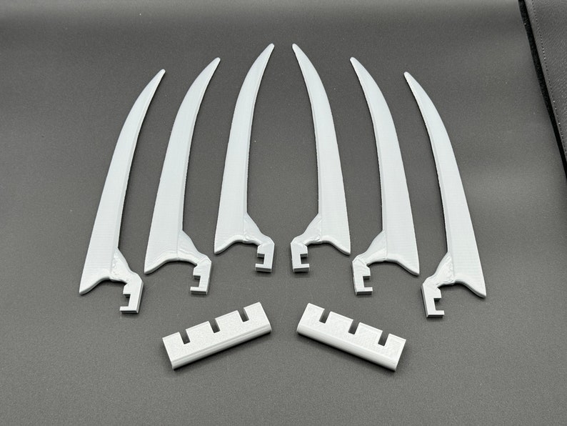 May include: Six white plastic claws with a textured surface and a curved shape. Two white plastic pieces with a textured surface and a rectangular shape.