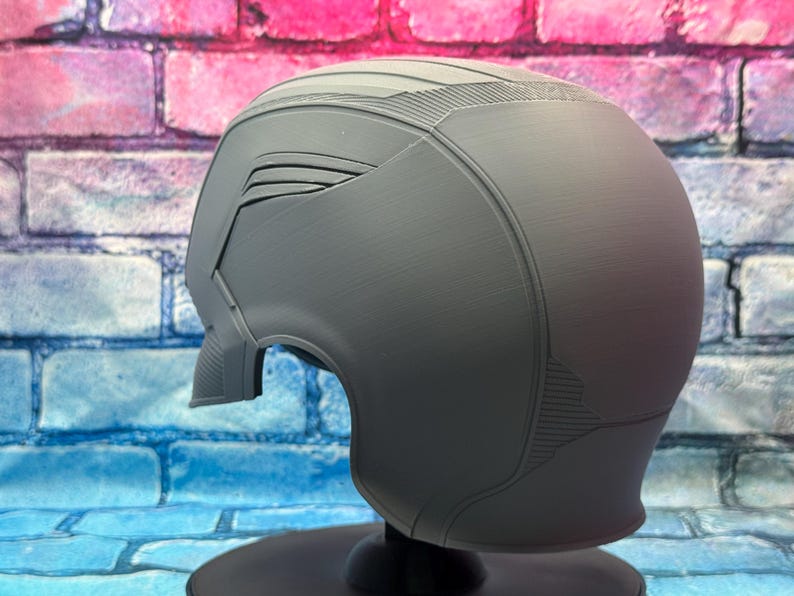 May include: A gray helmet with a futuristic design, featuring angular panels and textured surfaces. The helmet has a visor area and is mounted on a black stand. The overall aesthetic suggests a sci-fi or cosplay theme.