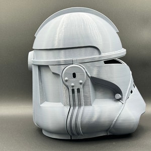 Puede incluir: Un casco gris impreso en 3D con un dise&ntilde;o detallado. El casco tiene una visera y una superficie texturizada.