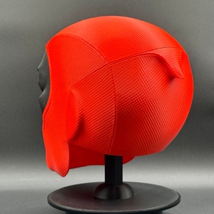 Puede incluir: M&aacute;scara de Deadpool impresa en 3D de color rojo y negro sobre un soporte negro. La m&aacute;scara tiene una superficie texturizada y est&aacute; dise&ntilde;ada para parecerse a la cabeza de Deadpool.