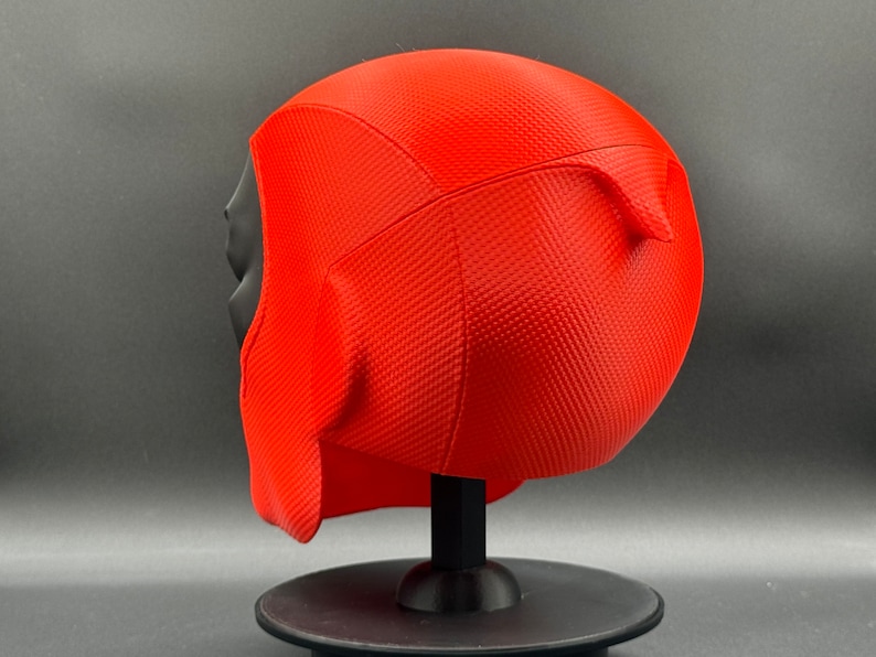 Puede incluir: M&aacute;scara de Deadpool impresa en 3D de color rojo y negro sobre un soporte negro. La m&aacute;scara tiene una superficie texturizada y est&aacute; dise&ntilde;ada para parecerse a la cabeza de Deadpool.