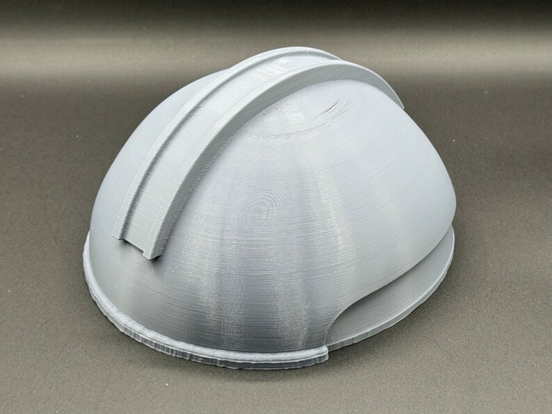 Puede incluir: Un casco gris impreso en 3D con una cresta elevada en la parte superior.