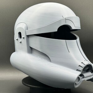May include: A white plastic helmet with a visor and a detailed design. The helmet has a rounded top and a long, curved chin piece.