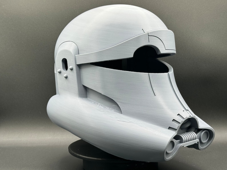 May include: A white plastic helmet with a visor and a detailed design. The helmet has a rounded top and a long, curved chin piece.