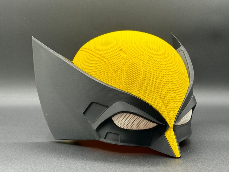 May include: A yellow and black plastic mask with a textured surface. The mask has a raised design on the forehead and a black eye mask with a white mesh.