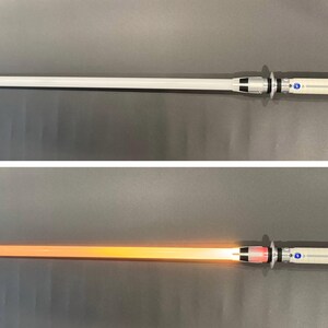 May include: A silver and white lightsaber with a glowing orange blade. The hilt features silver and black accents with blue and red buttons. The lightsaber is shown both on and off, with the blade illuminated in the on position.