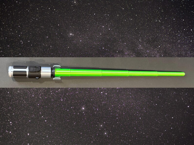 May include: A green lightsaber prop with a black and silver handle. The lightsaber is a toy or collectible item, likely from a science fiction franchise. The background is a starry night sky.