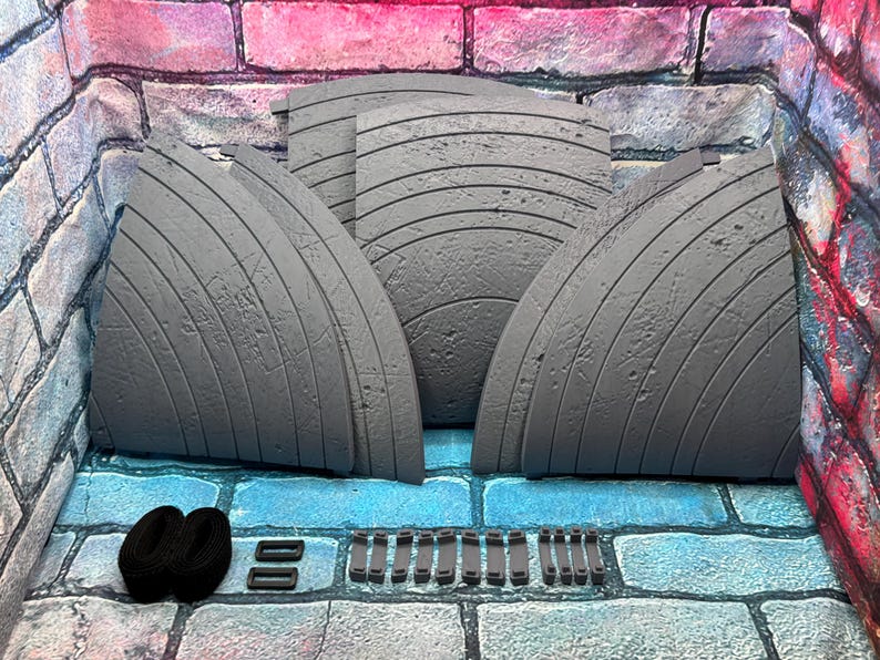 May include: A set of gray, curved, textured panels with horizontal lines, possibly for a diorama or display. Also included are black straps and small rectangular pieces. The items are arranged on a blue and gray brick surface, with a brick wall backdrop.