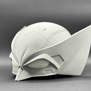 Puede incluir: Un casco blanco impreso en 3D con un dise&ntilde;o detallado, que incluye una pieza de ojo de malla y una forma puntiaguda y angular.