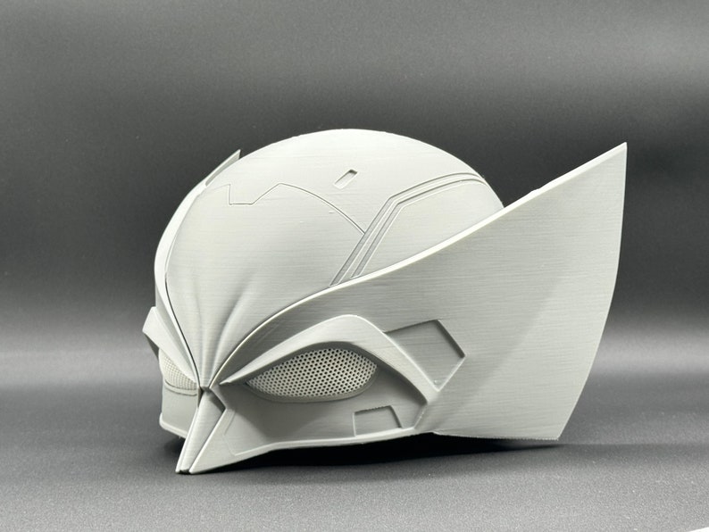 Puede incluir: Un casco blanco impreso en 3D con un dise&ntilde;o detallado, que incluye una pieza de ojo de malla y una forma puntiaguda y angular.
