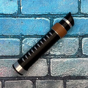 May include: A black and silver decorative object with a brown band and white accents. The object has a cylindrical shape with a pointed end and is set against a blue brick wall background.