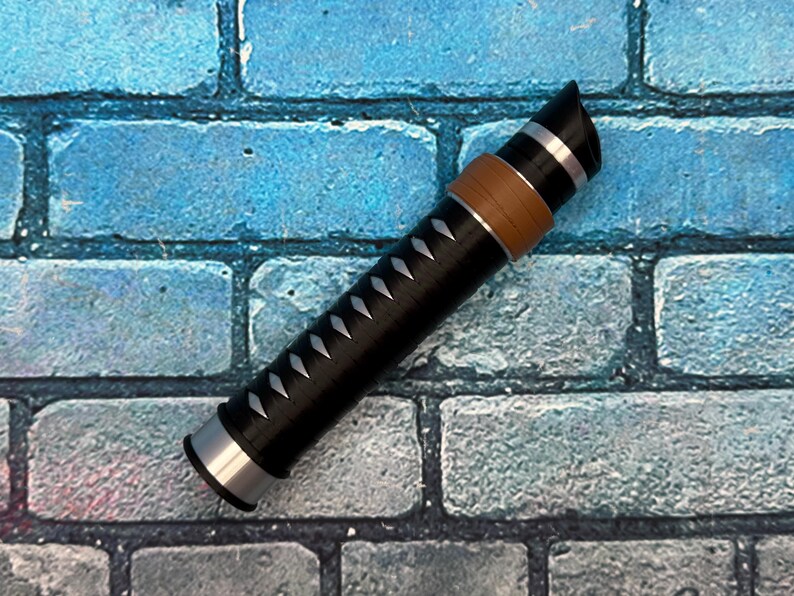 May include: A black and silver decorative object with a brown band and white accents. The object has a cylindrical shape with a pointed end and is set against a blue brick wall background.