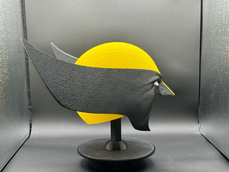 Puede incluir: Una m&aacute;scara de Wolverine impresa en 3D de color amarillo y negro sobre un soporte negro. La m&aacute;scara tiene una superficie texturizada y est&aacute; dise&ntilde;ada para parecerse al rostro del personaje.