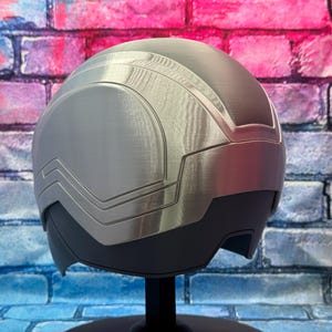 May include: A silver and black helmet with a futuristic design. The helmet has a smooth, metallic finish with angular panels and a visor area. The design suggests a sci-fi or cosplay theme.