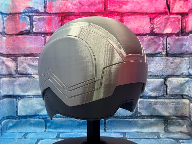 May include: A silver and black helmet with a futuristic design. The helmet has a smooth, metallic finish with angular panels and a visor area. The design suggests a sci-fi or cosplay theme.
