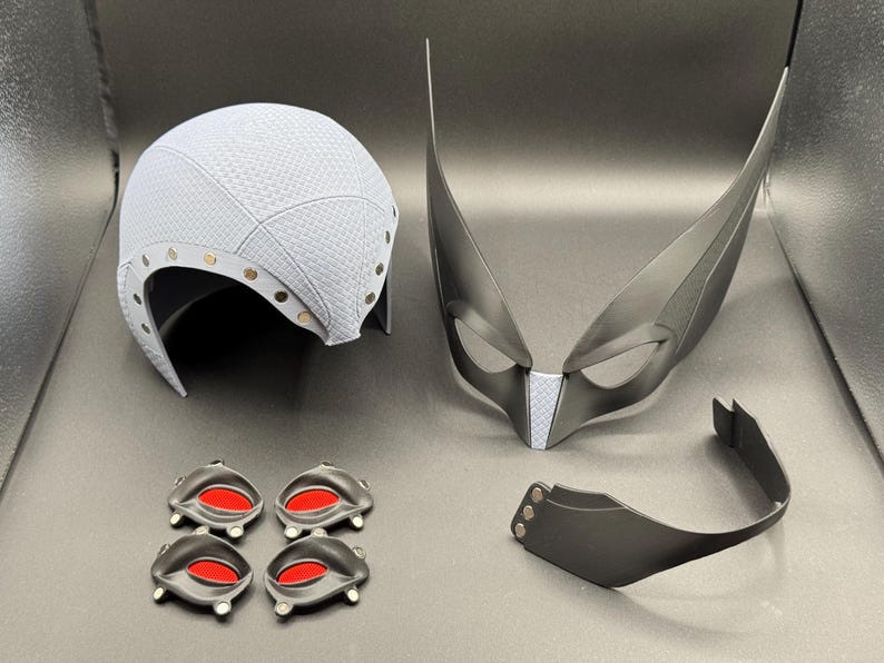 May include: A set of costume accessories including a white helmet, a black mask with white accents, a black headband, and four black eye pieces with red accents.